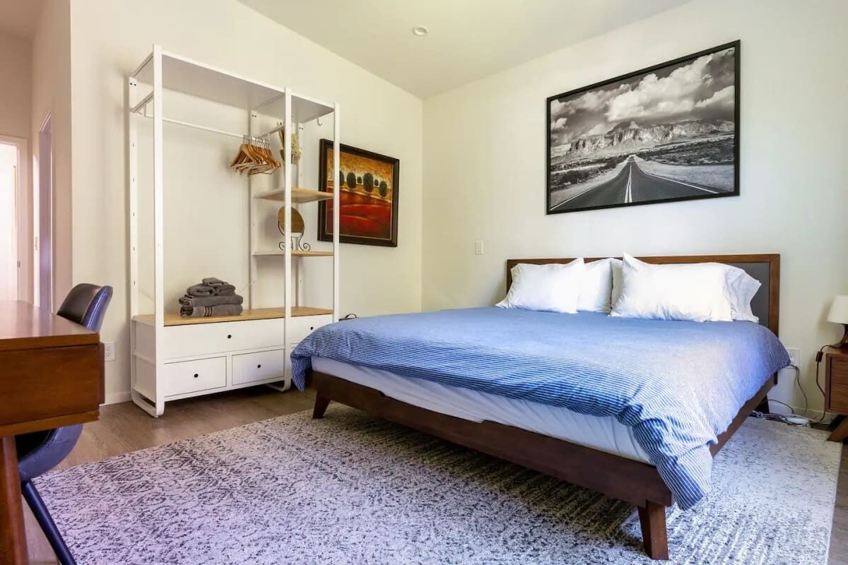 Quarto com cama, guarda-roupa, escrivaninha e um quadro na parede.