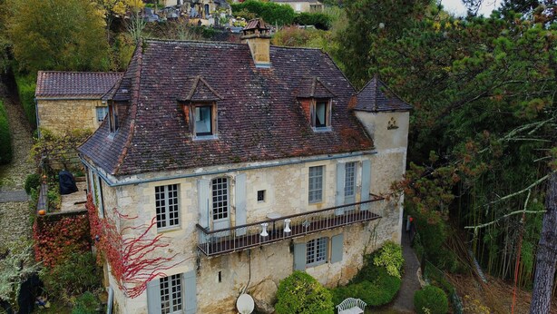 Un edificio storico in pietra con un tetto ripido, diverse finestre e un piccolo balcone.