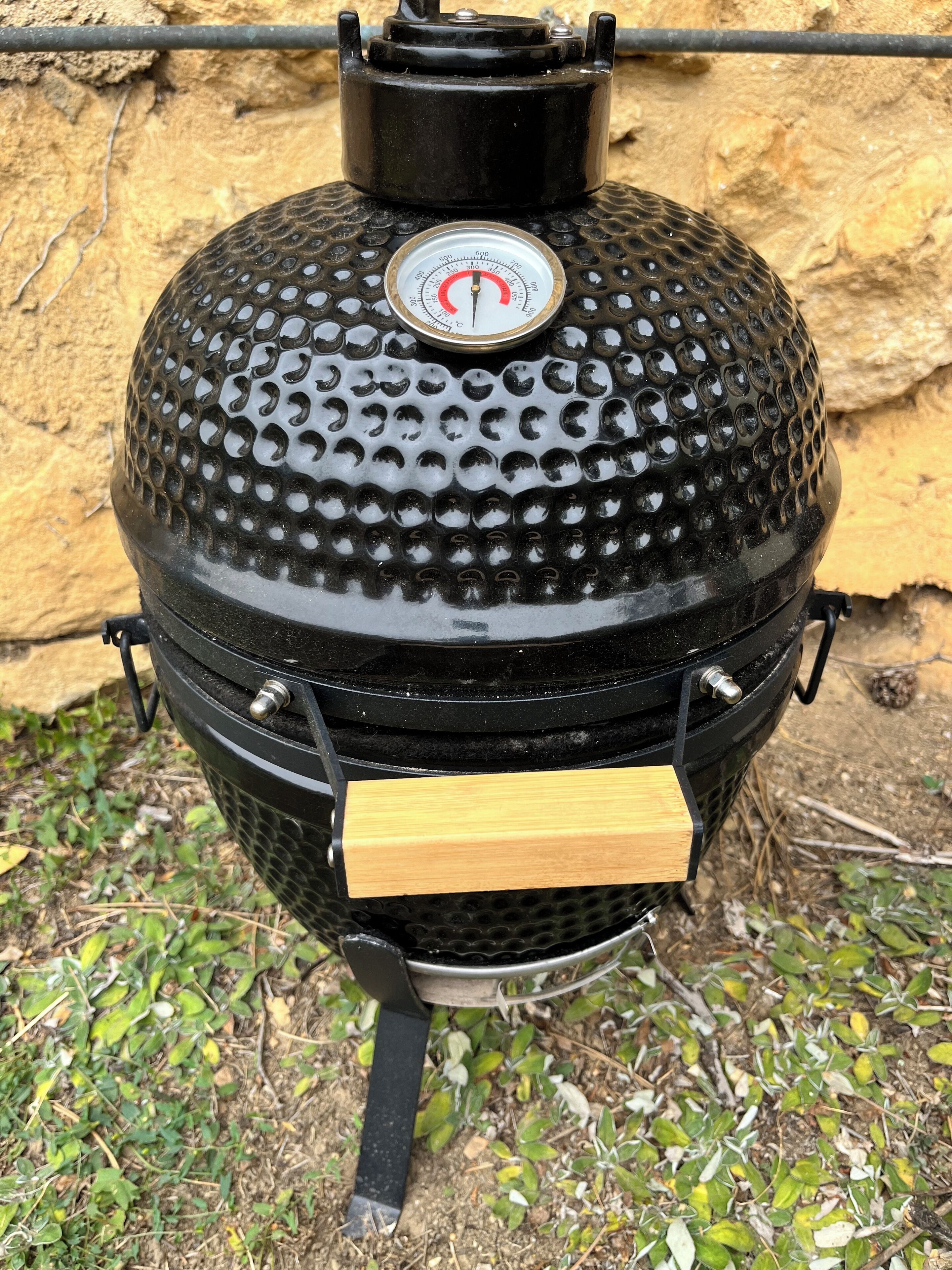 Un barbecue noir doté d’un thermomètre, d’un manche en bois et d’une grille d’aération en métal.