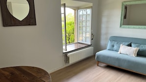 Una stanza con un tavolo in legno, un divano blu con un cuscino bianco, uno specchio a forma di cuore e una finestra con vista sul verde.