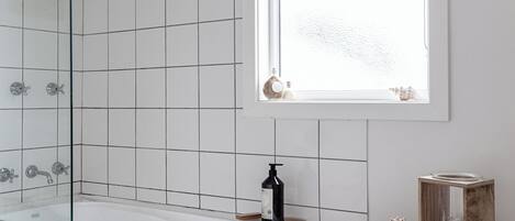 A modern bathroom with a glass-enclosed shower, a large bathtub, and a window providing natural light.