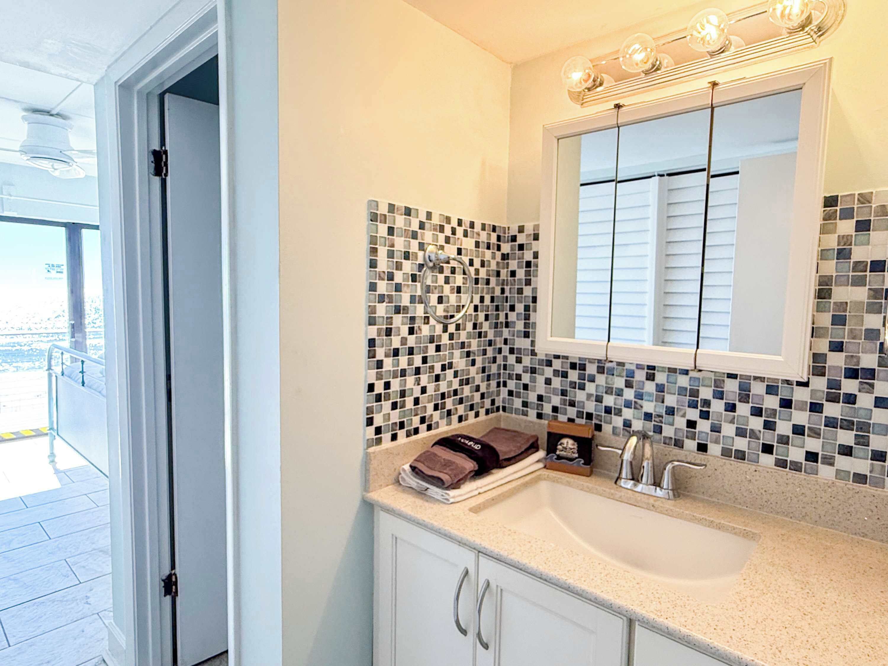 A bathroom with a tiled backsplash, a sink, and a mirror.