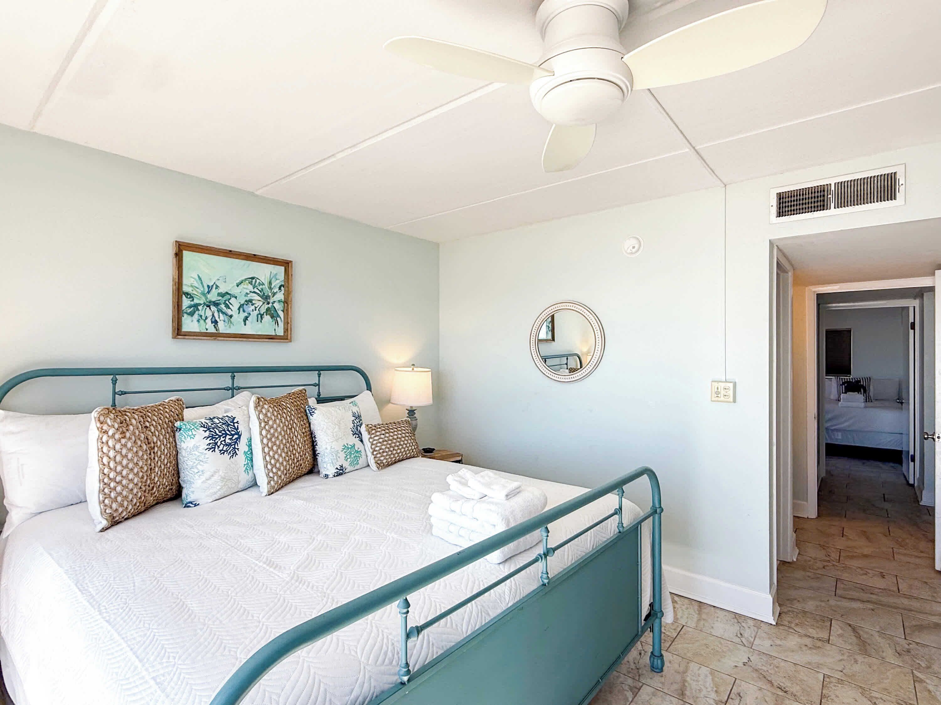 A bedroom with a bed, a ceiling fan, a mirror, and a door leading to another room.