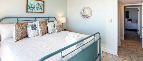 A bedroom with a bed, a ceiling fan, a mirror, and a door leading to another room.
