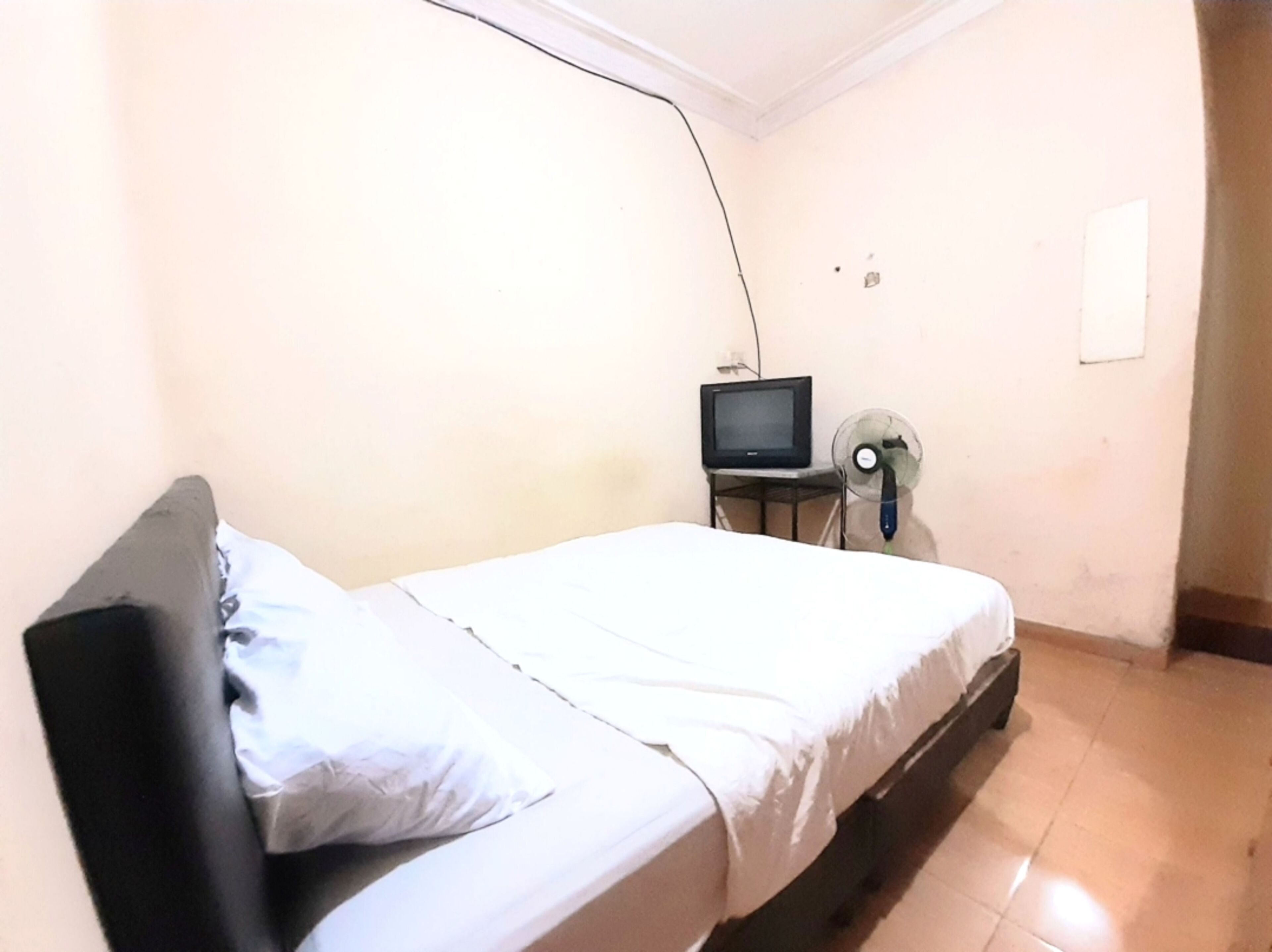 Een enkel bed met een witte matras en een zwart hoofdeinde in een kamer met een betegelde vloer.