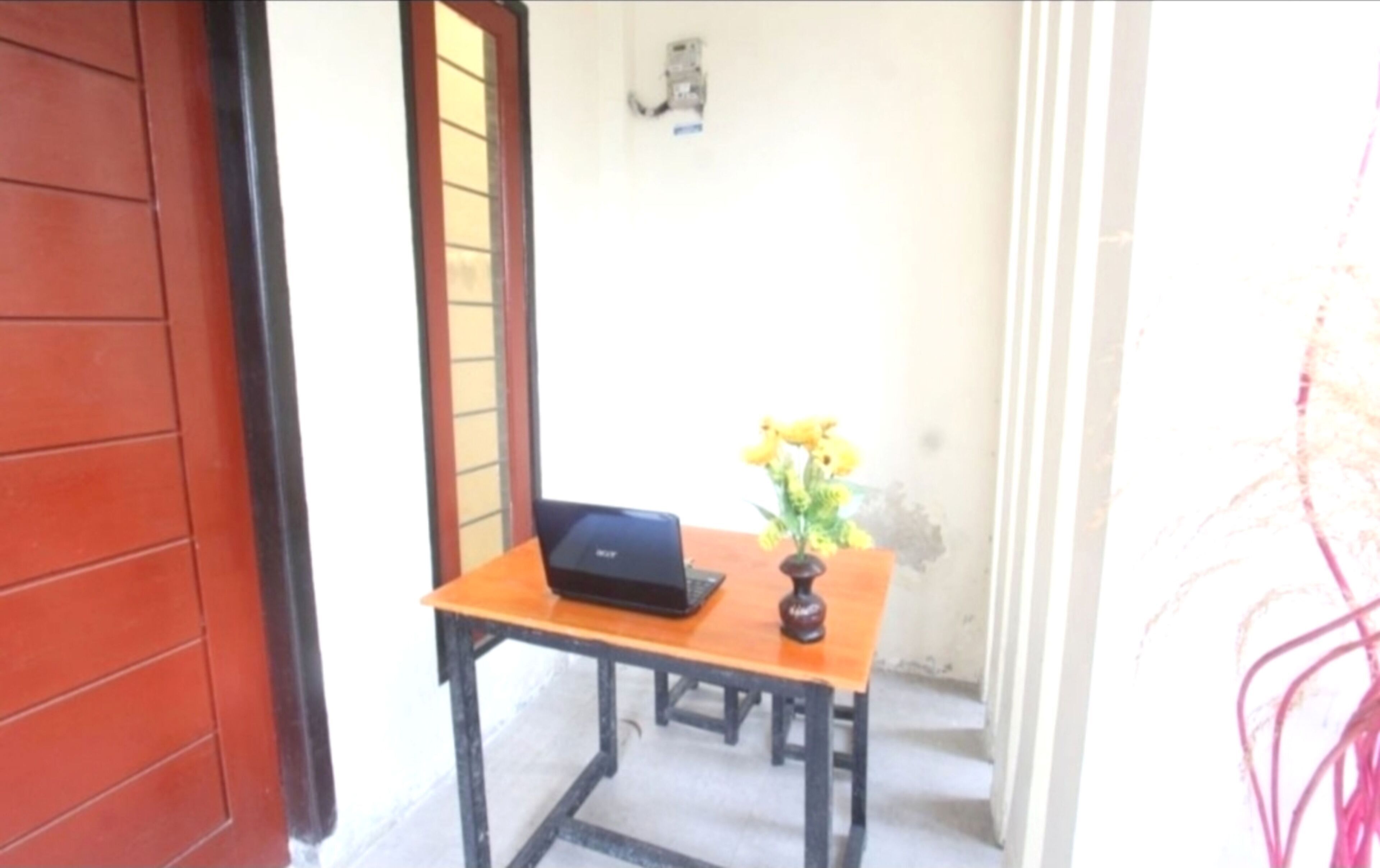 A small wooden table with a laptop and a vase of yellow flowers.