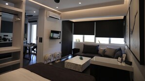 A modern living room with a sofa, coffee table, and a TV. There is a kitchen area with a dining table and chairs visible.