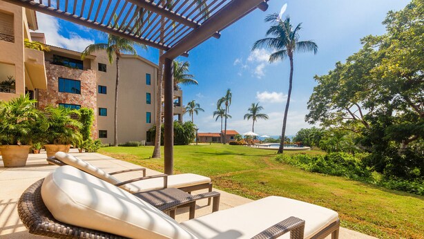 A resort with outdoor seating, palm trees, and a pool in the background. - Perfect 4 Bedroom Condo (Punta de Mita)