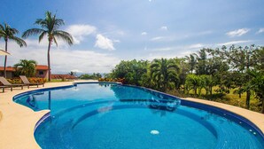 A large, clear blue swimming pool with a curved edge, surrounded by palm trees and a clear sky. - Perfect 4 Bedroom Condo (Punta de Mita)
