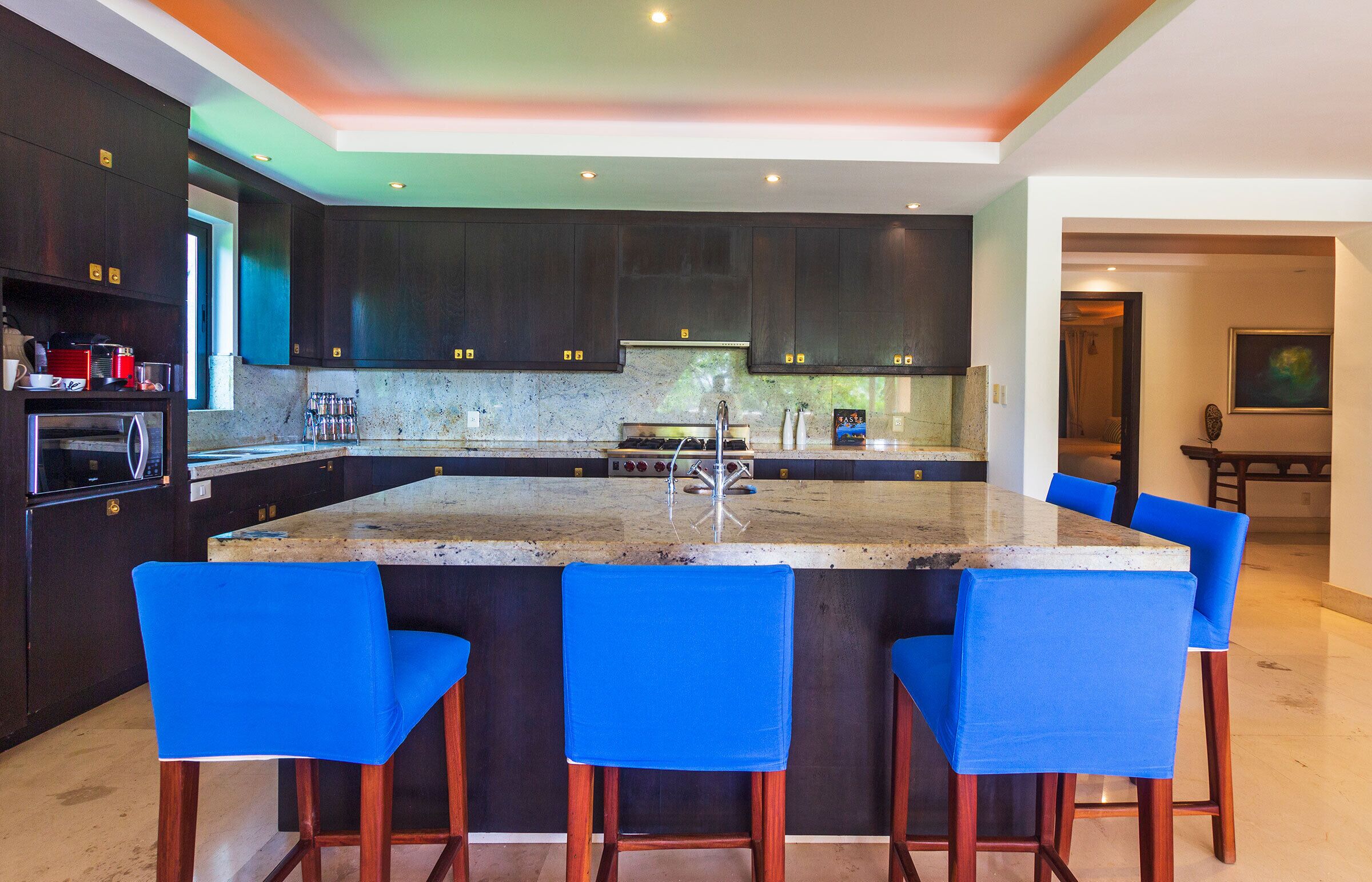 A modern kitchen with dark cabinets, a large island with bar stools, and a stainless steel sink.