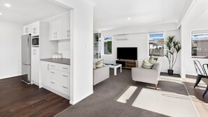 A modern apartment with a kitchen, living area, and balcony. - Mount Maunganui Beach House Family Friendly (Mount Maunganui)