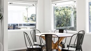 A dining area with a round table, four chairs, and large windows. - Mount Maunganui Beach House Family Friendly (Mount Maunganui)