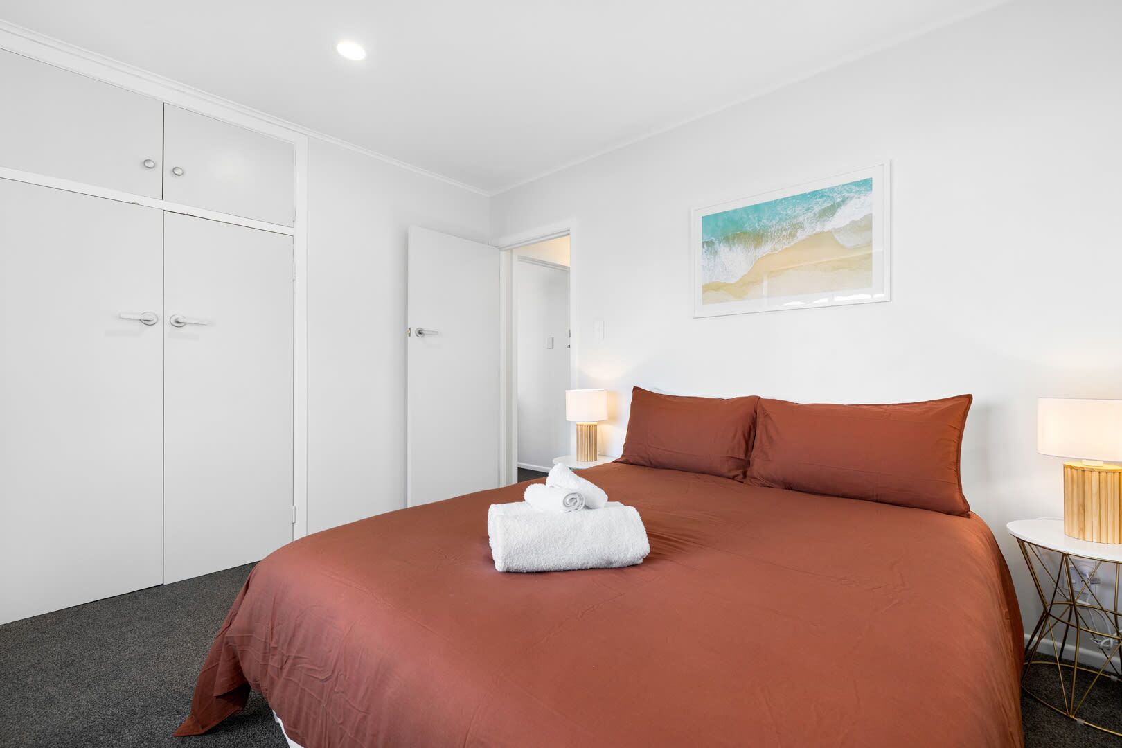 A hotel room with a large bed, white wardrobe, and a painting on the wall.