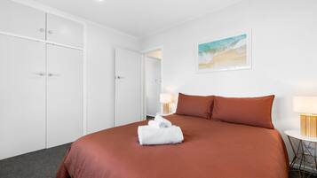 A hotel room with a large bed, white wardrobe, and a painting on the wall.