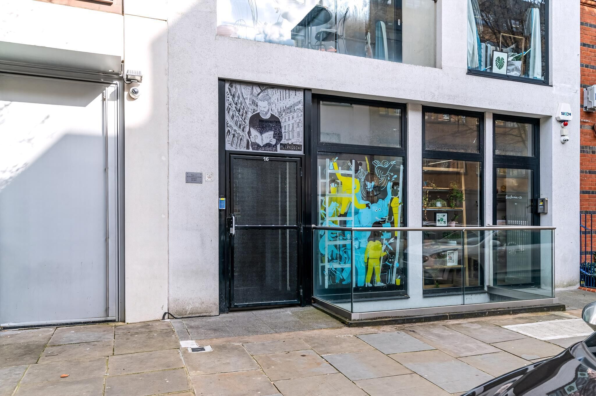 A building with a glass storefront, a black door, and a window with a colorful mural.