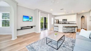A modern living room with a grey sofa, a coffee table, and a TV mounted on the wall. - Upstay Pet-Friendly Condo Near Disney w Balcony (Winter Garden)