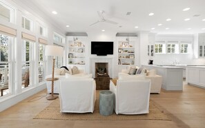A spacious living room with a fireplace, white furniture, and large windows.