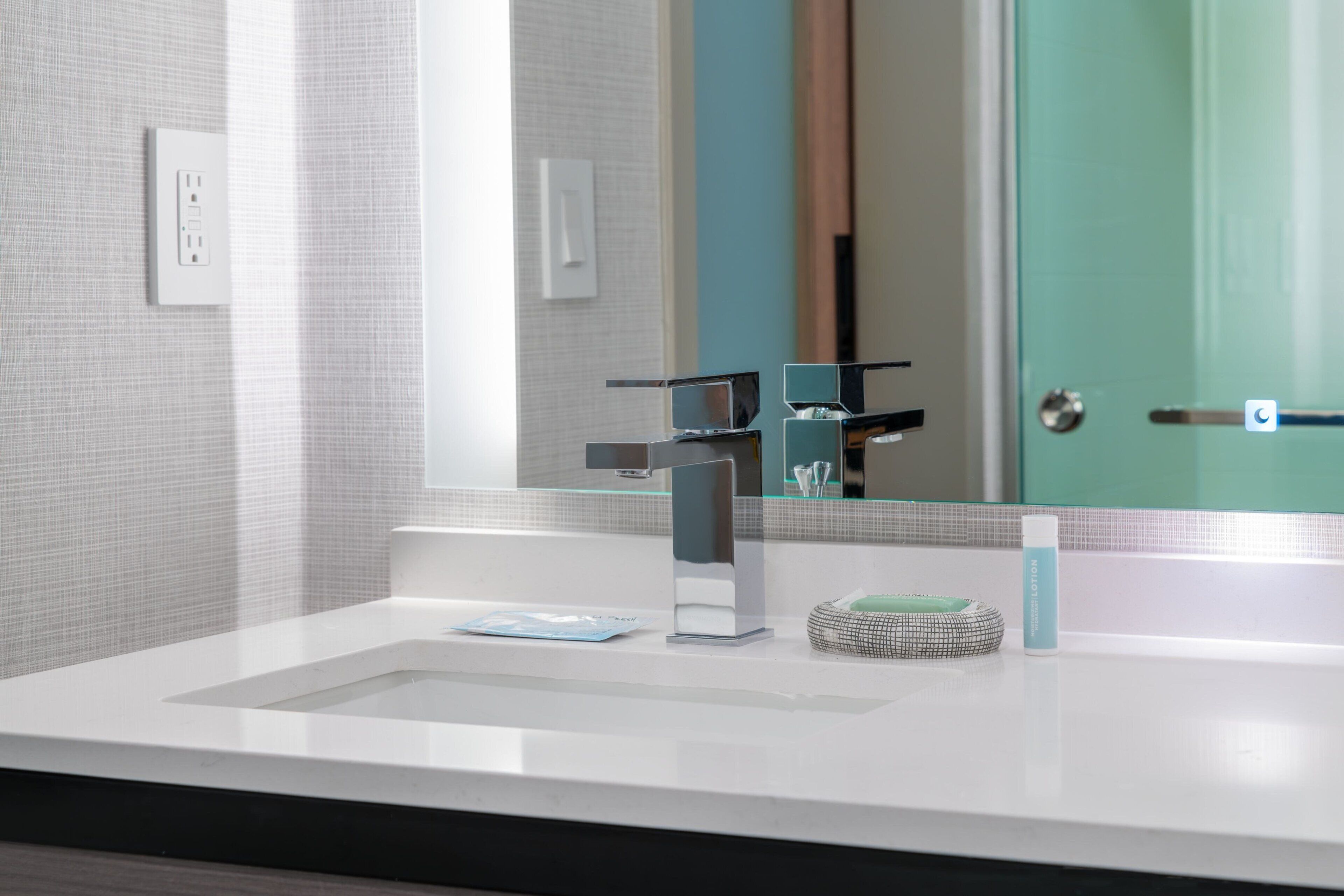 Un baño moderno con un mostrador blanco, un espejo rectangular y una cabina de ducha de vidrio.