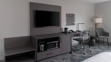 A modern hotel room with a flat-screen TV mounted on the wall, a desk with a chair, a microwave, and a small cabinet.