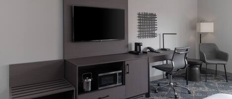 Una habitación de hotel moderna con una televisión de pantalla plana montada en la pared, un escritorio con una silla, un microondas y un mueble auxiliar.