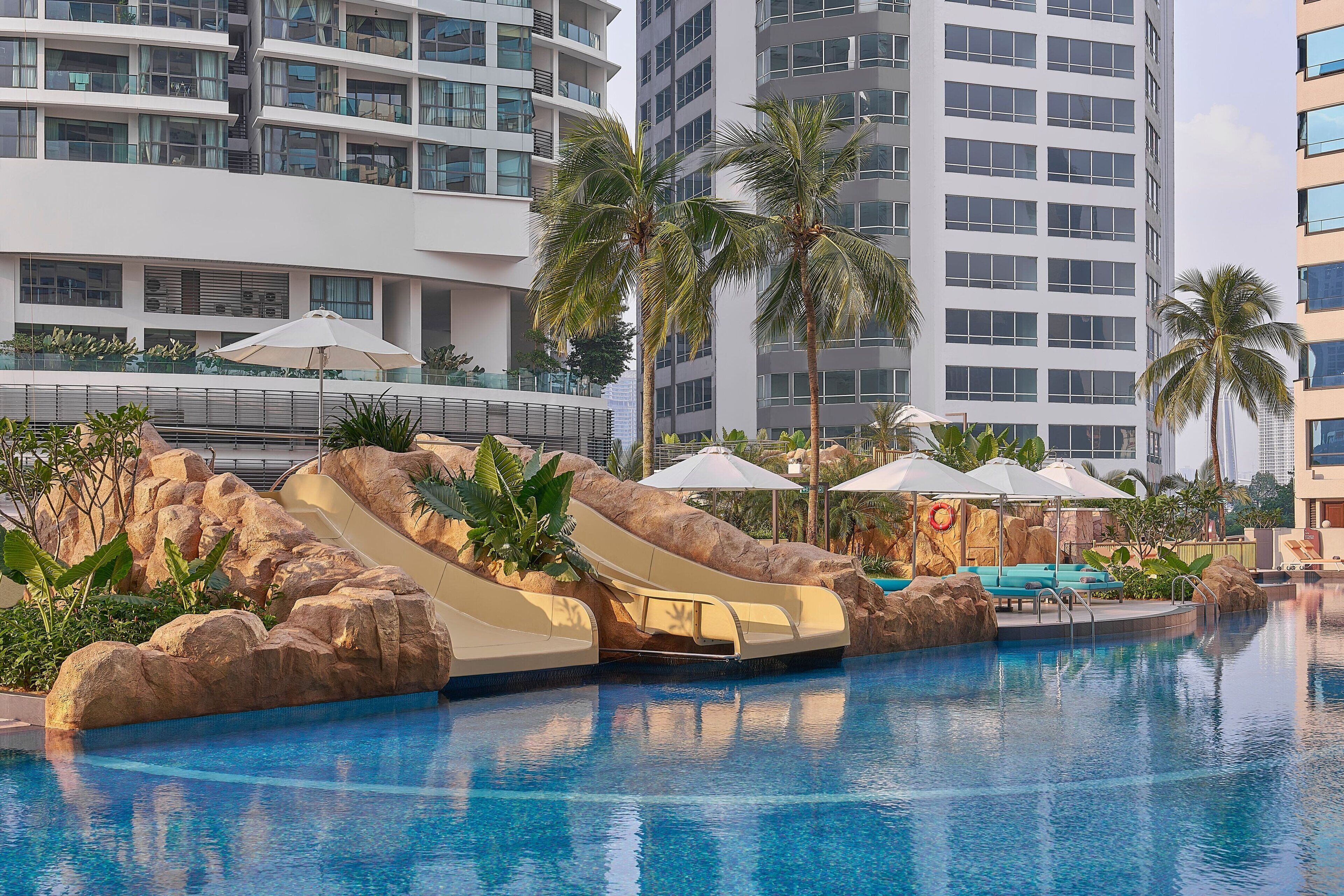 A swimming pool with slides, palm trees, and lounge chairs.