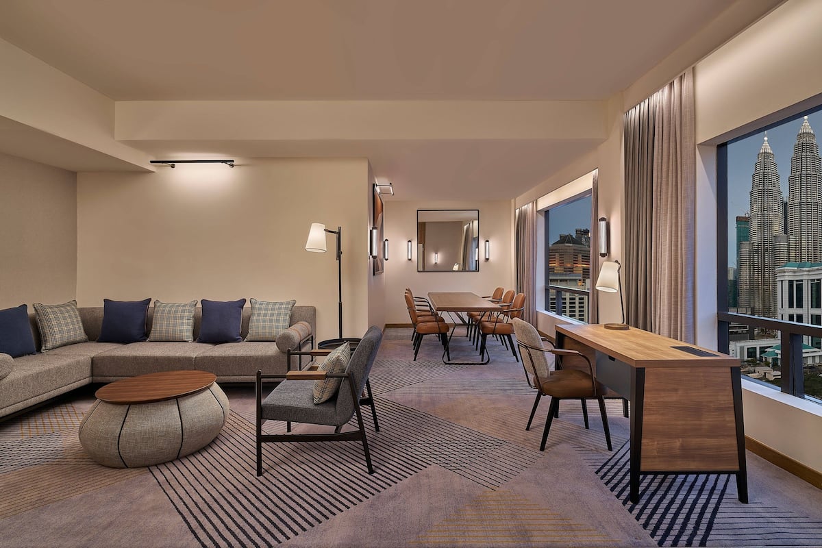 Een moderne hotelkamer met een zithoek, eethoek en een groot raam met uitzicht op de stad.
