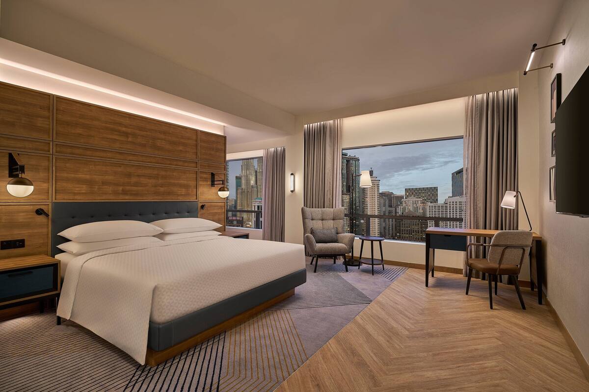 Een moderne hotelkamer met een groot bed, een bureau, een stoel en uitzicht op de stad.