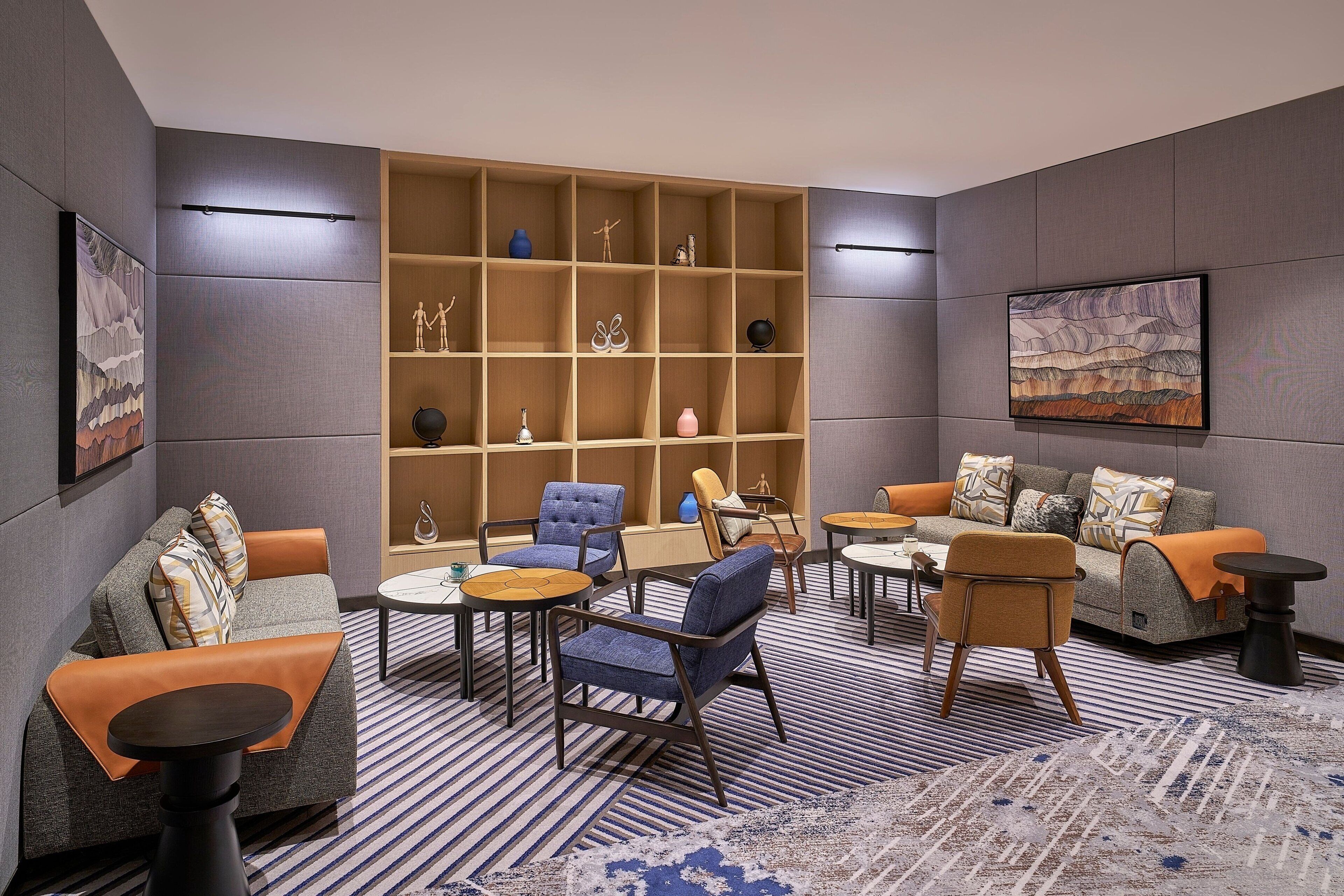 A modern lounge area with sofas, chairs, a bookshelf, and artwork on the walls.