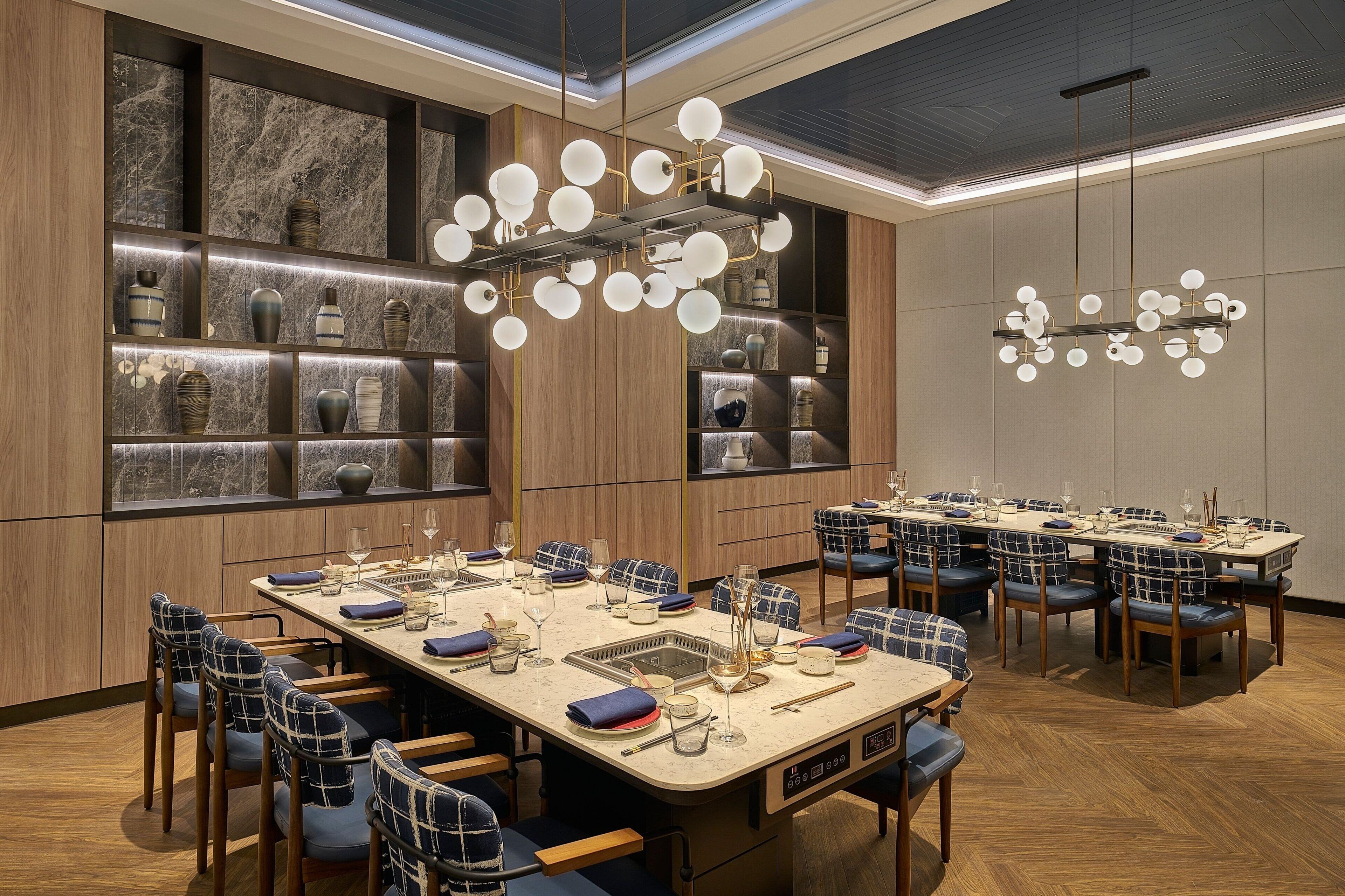 A modern dining area with multiple tables, chairs, and a decorative chandelier.