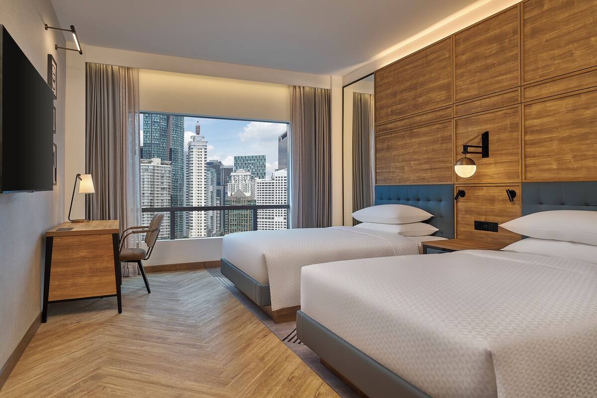 Hotelkamer met twee bedden, een bureau, een stoel, een televisie en uitzicht over de stad.