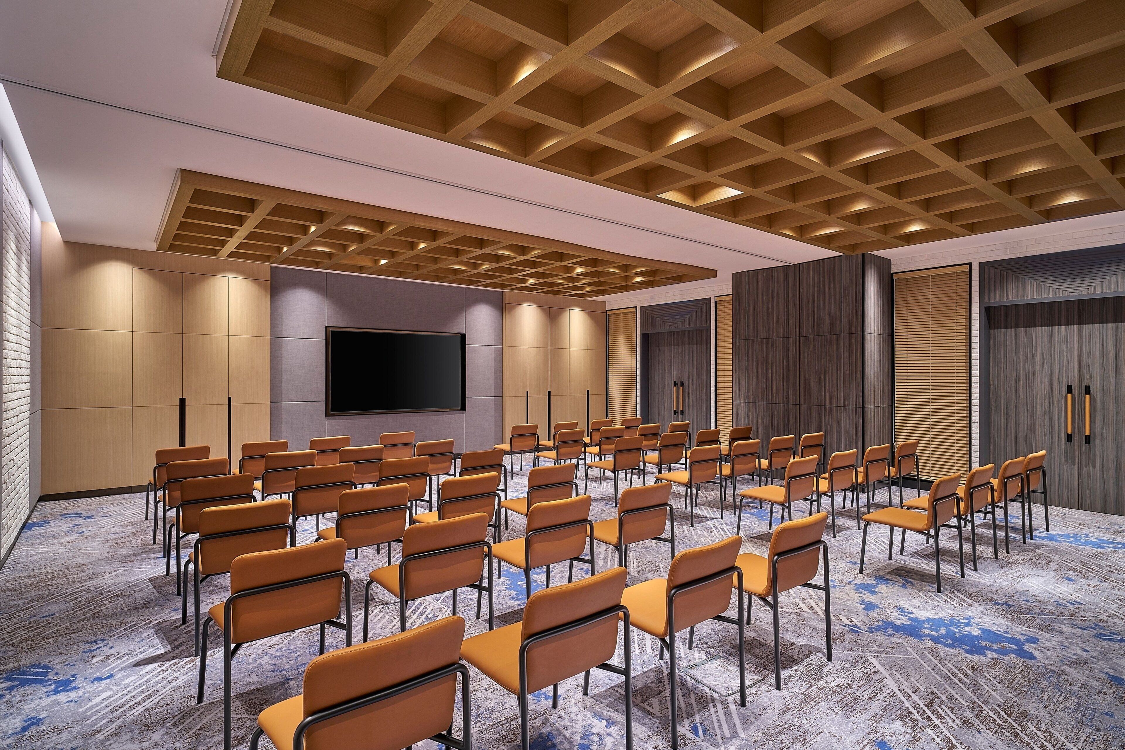 A conference room with rows of chairs, a large screen, and a patterned carpet.