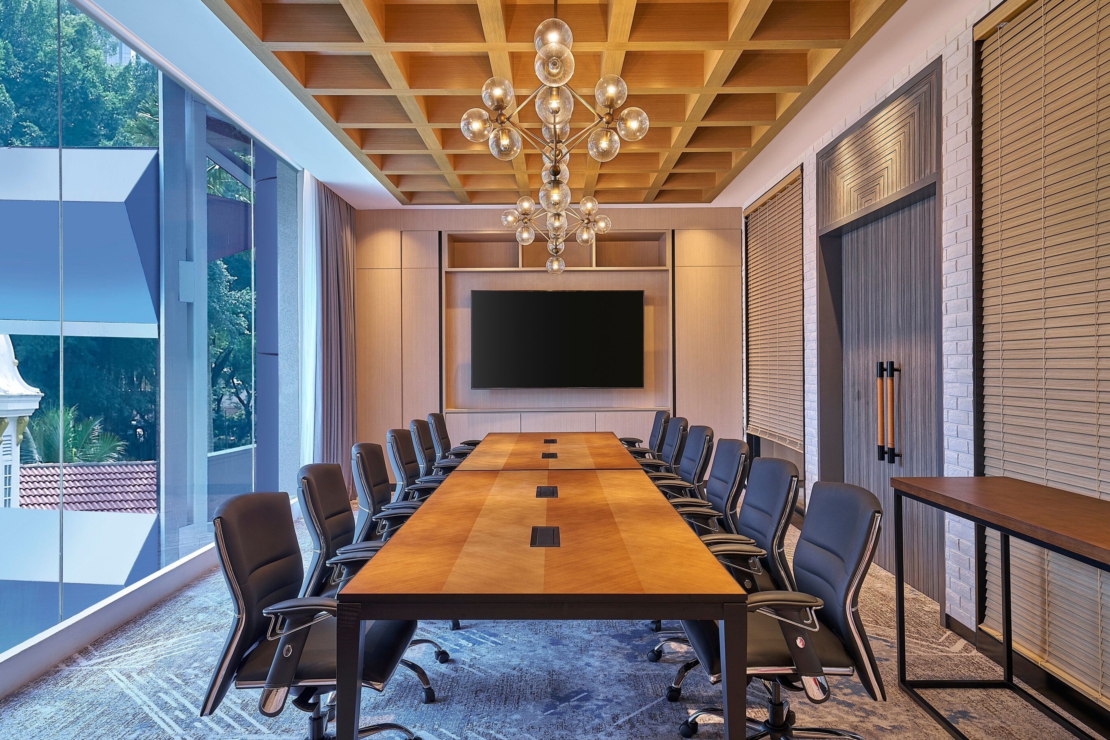 A conference room with a long table, chairs, a large screen, and a chandelier.