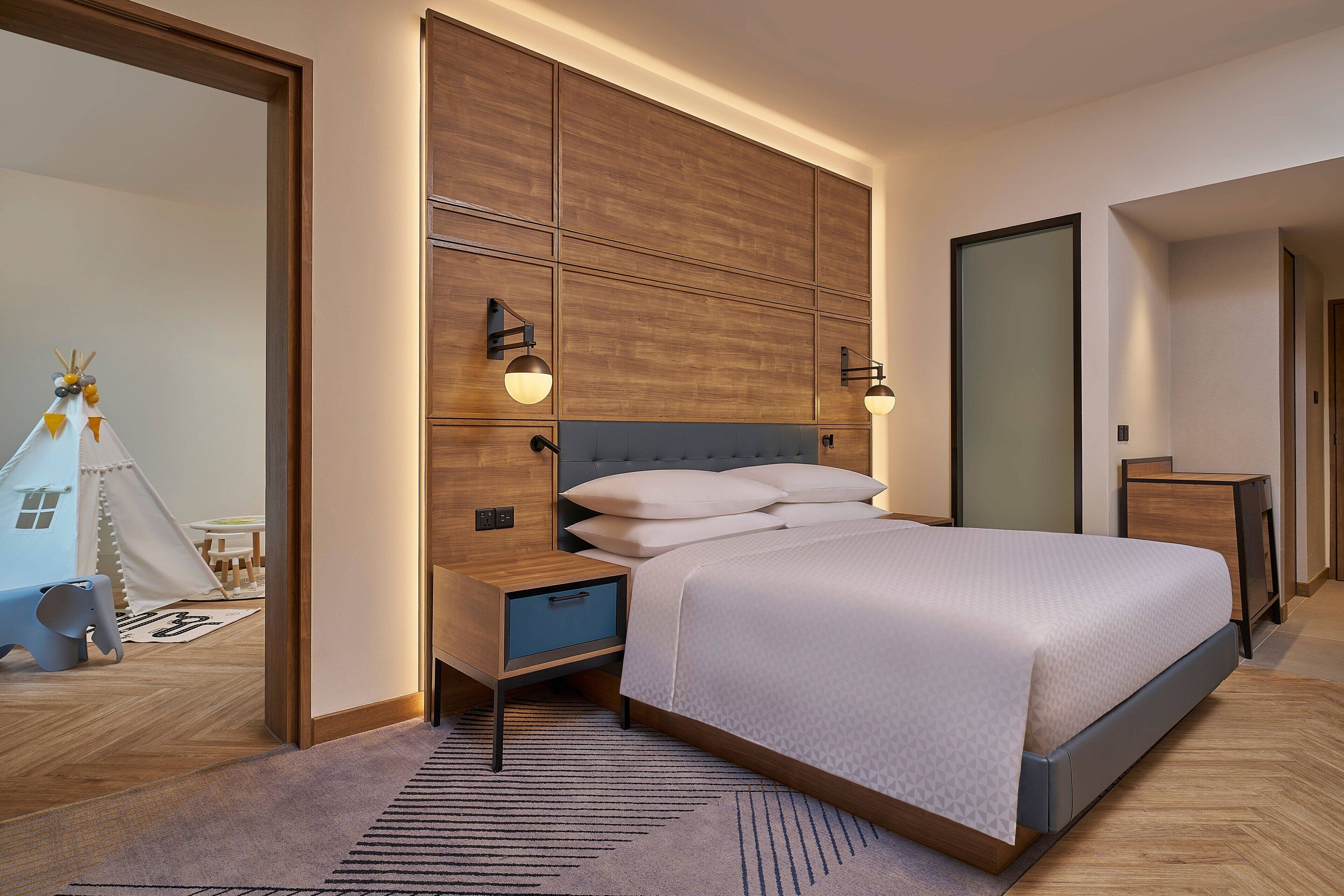 A modern bedroom with a large bed, bedside tables, a nightstand, and a wall-mounted light fixture.