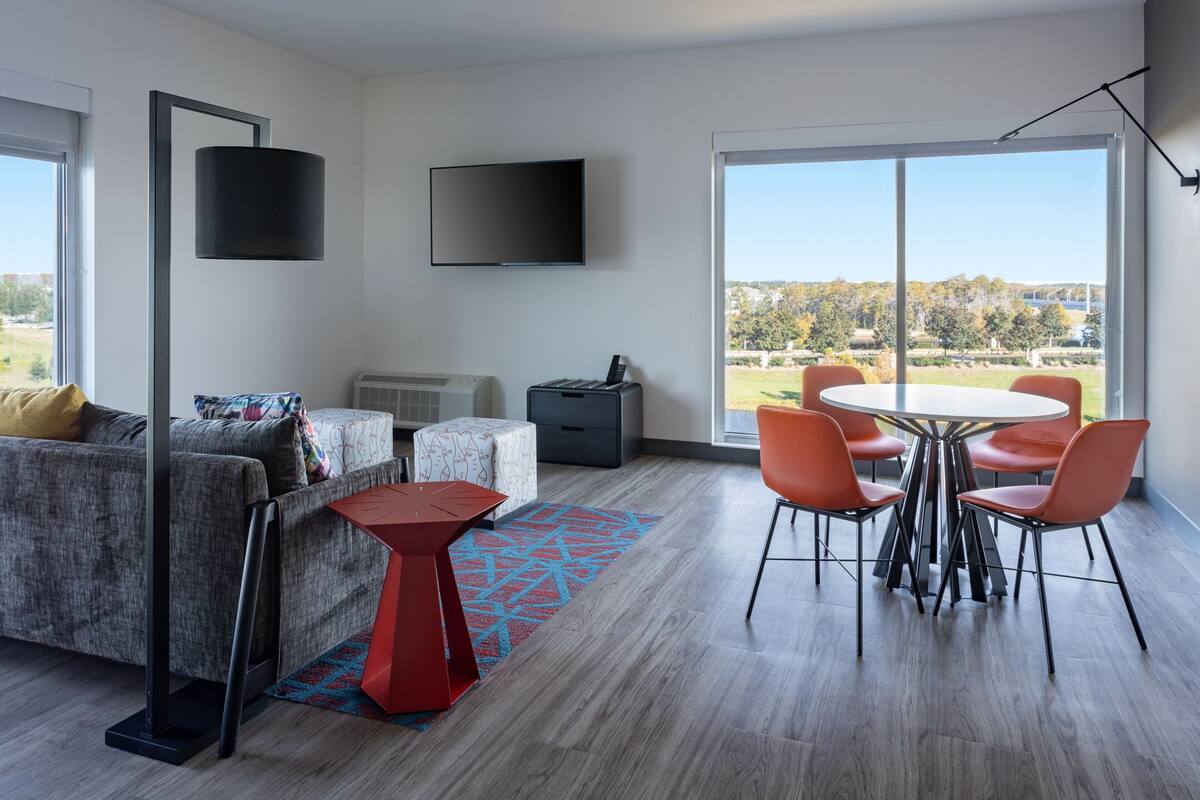 A modern living room with a sofa, a coffee table, a TV, and a dining area with chairs and a table.