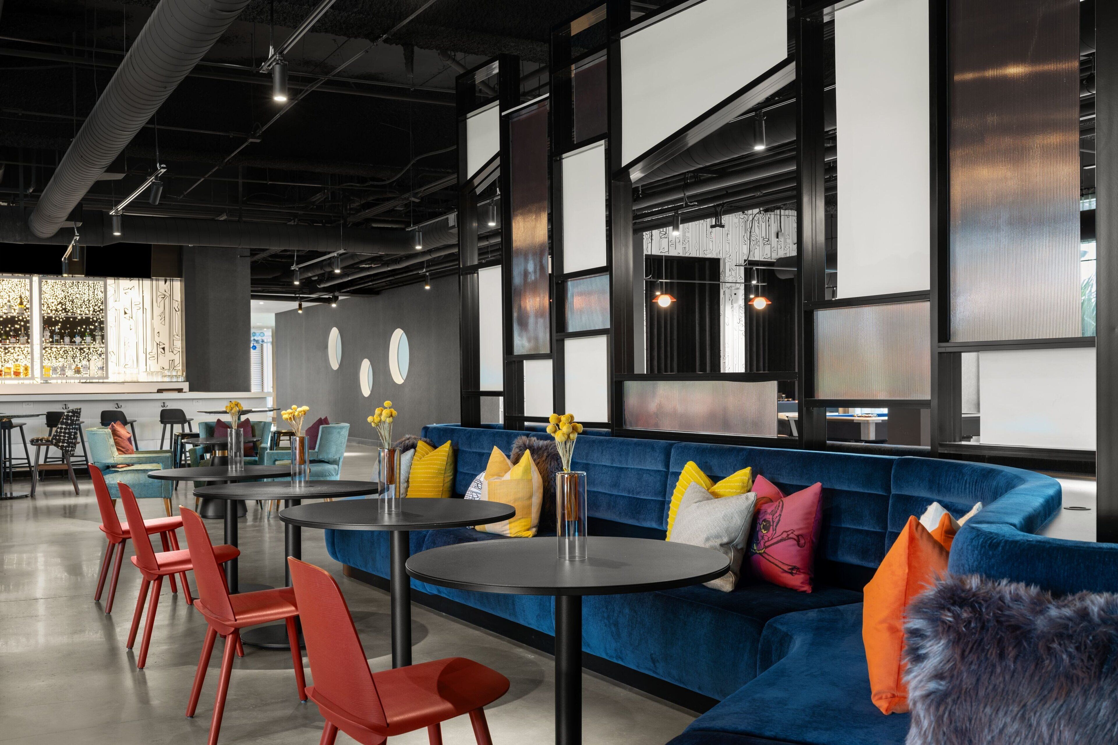 A modern lounge area with a blue sofa, red chairs, and round tables.