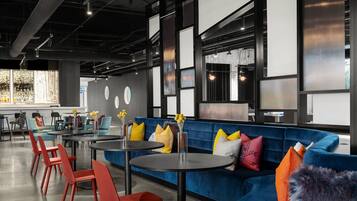A modern lounge area with a blue sofa, red chairs, and round tables.