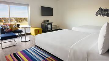 A hotel room with a large bed, a TV mounted on the wall, a small table, and a sofa with a colorful rug.