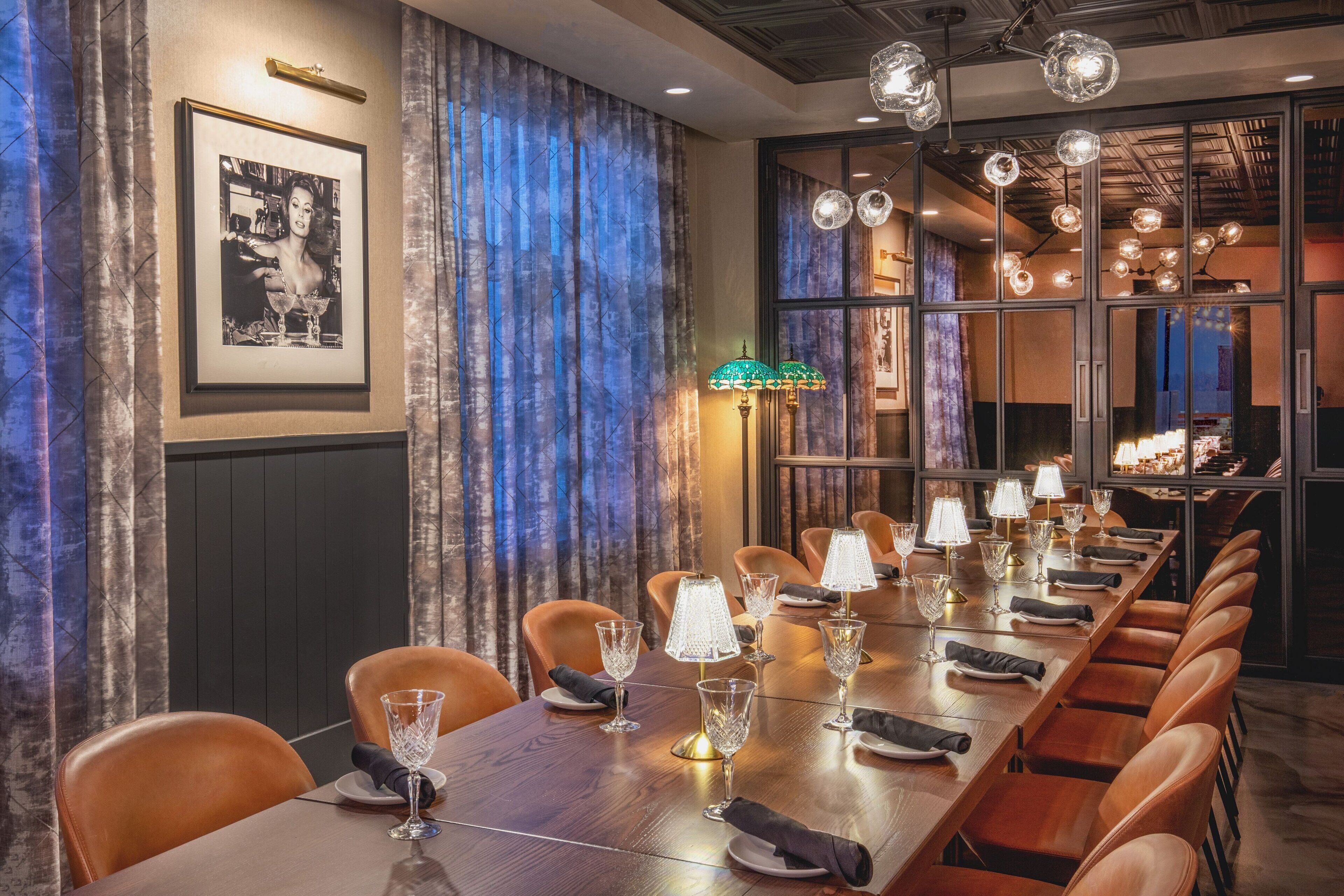 A long dining table with multiple chairs, lit by crystal chandeliers and table lamps.