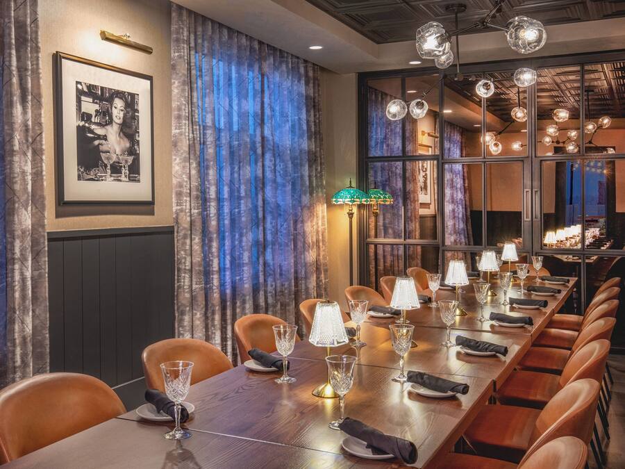 A long dining table with multiple chairs, lit by crystal chandeliers and table lamps.
