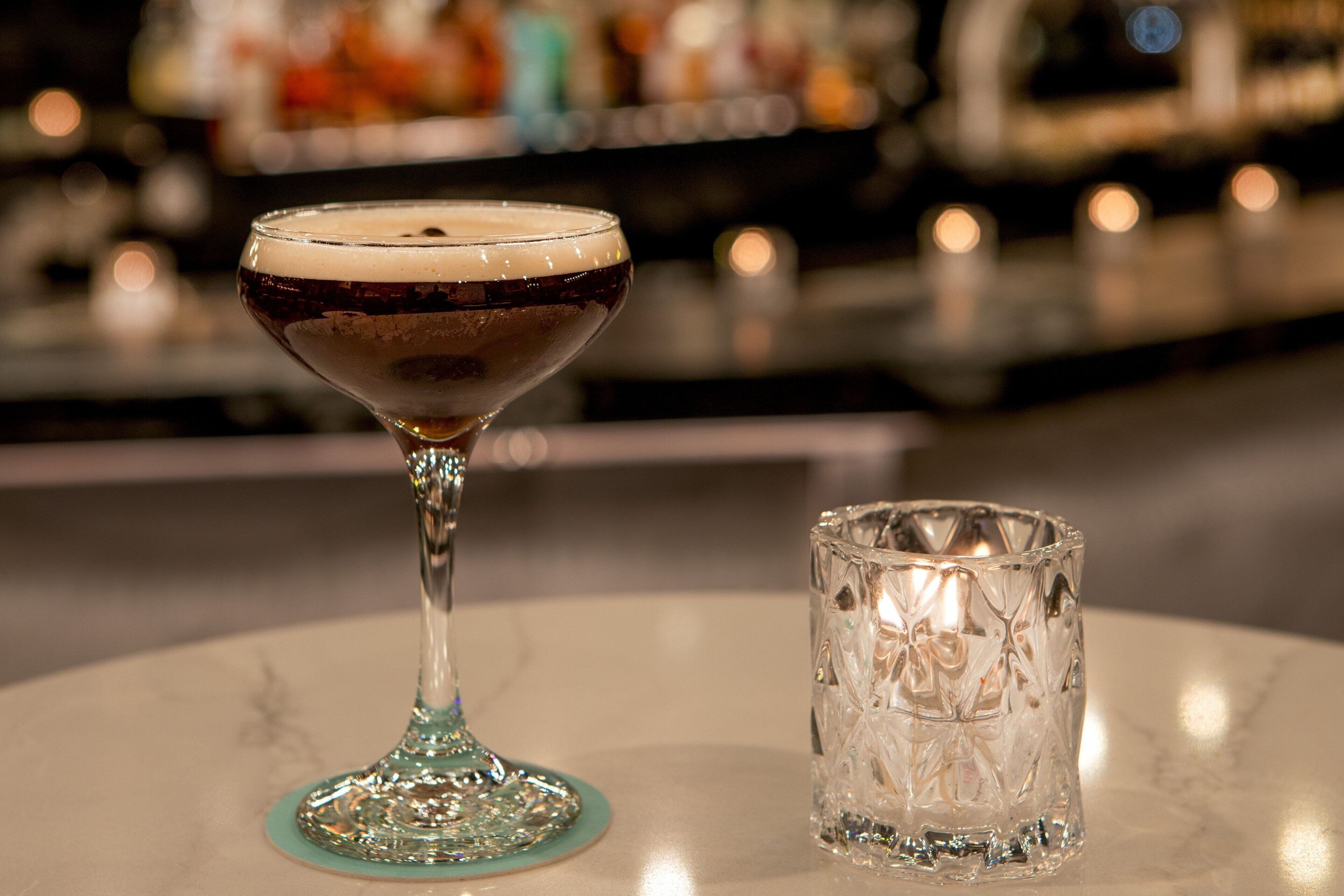Un bar con un cocktail in un bicchiere da vino e un bicchiere lavorato accanto.