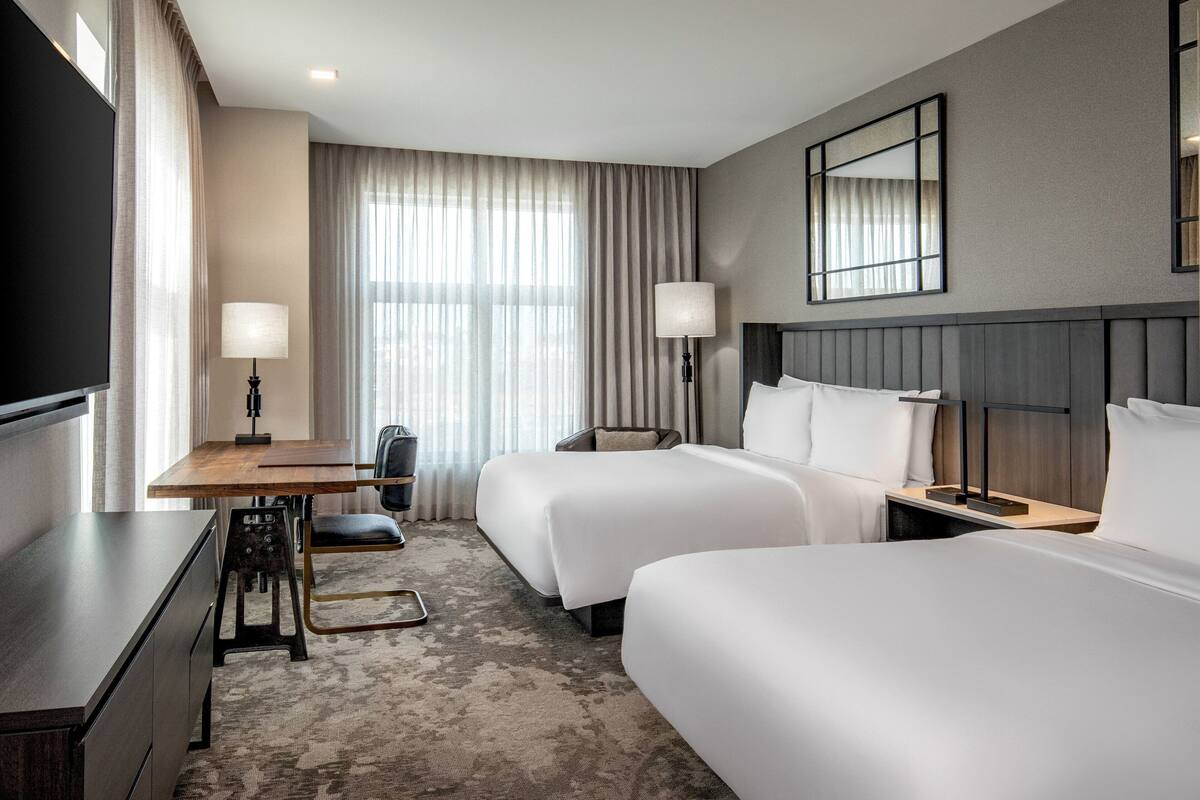 Une chambre d’hôtel avec deux lits, un bureau, une chaise et un téléviseur.