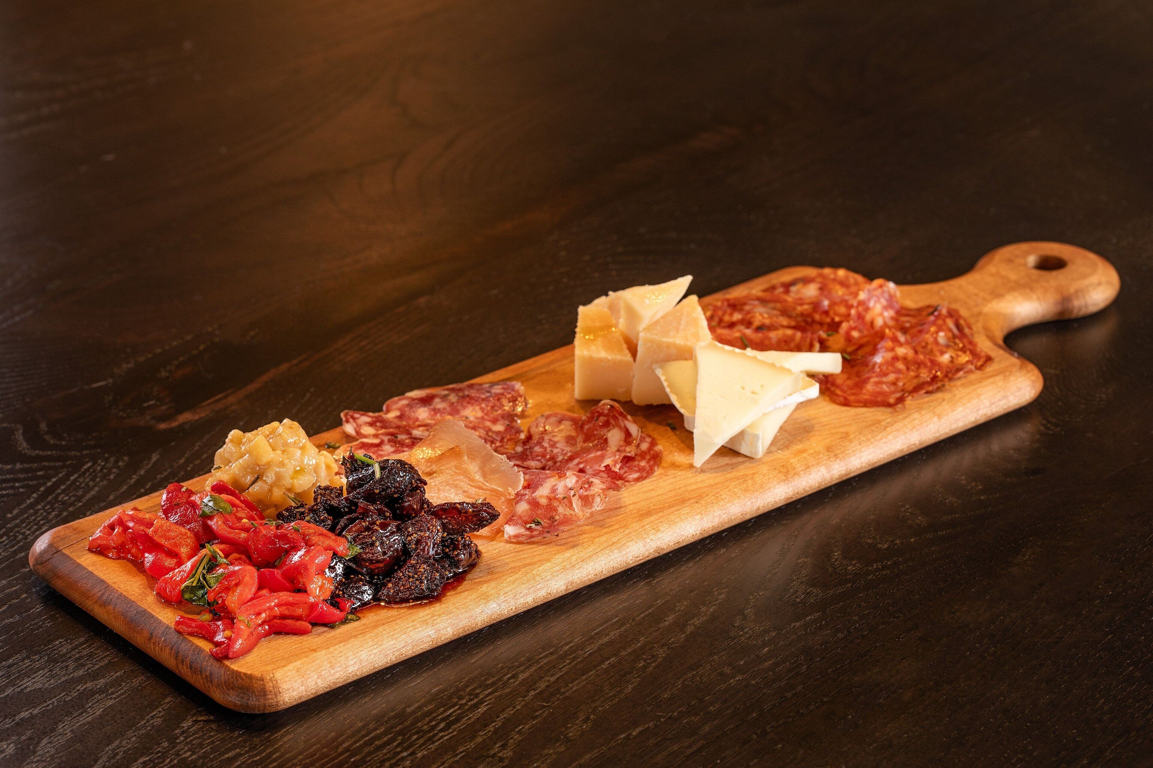 A wooden board with various cheeses, cured meats, and pickled vegetables.