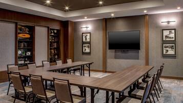 Una sala de conferencias con una mesa larga, sillas, un televisor de pantalla plana, cuadros enmarcados y una estantería.