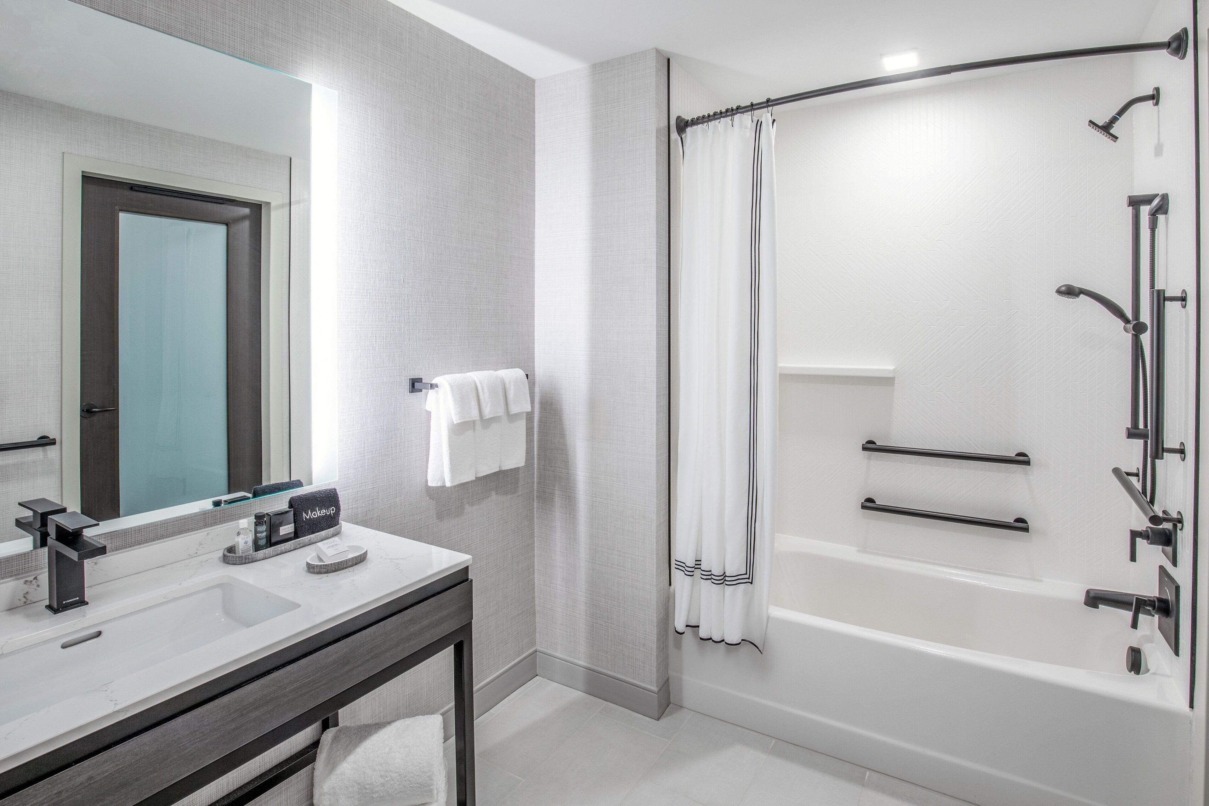 A modern bathroom with a large mirror, a sink, a vanity, a shower with a curtain, and a bathtub.