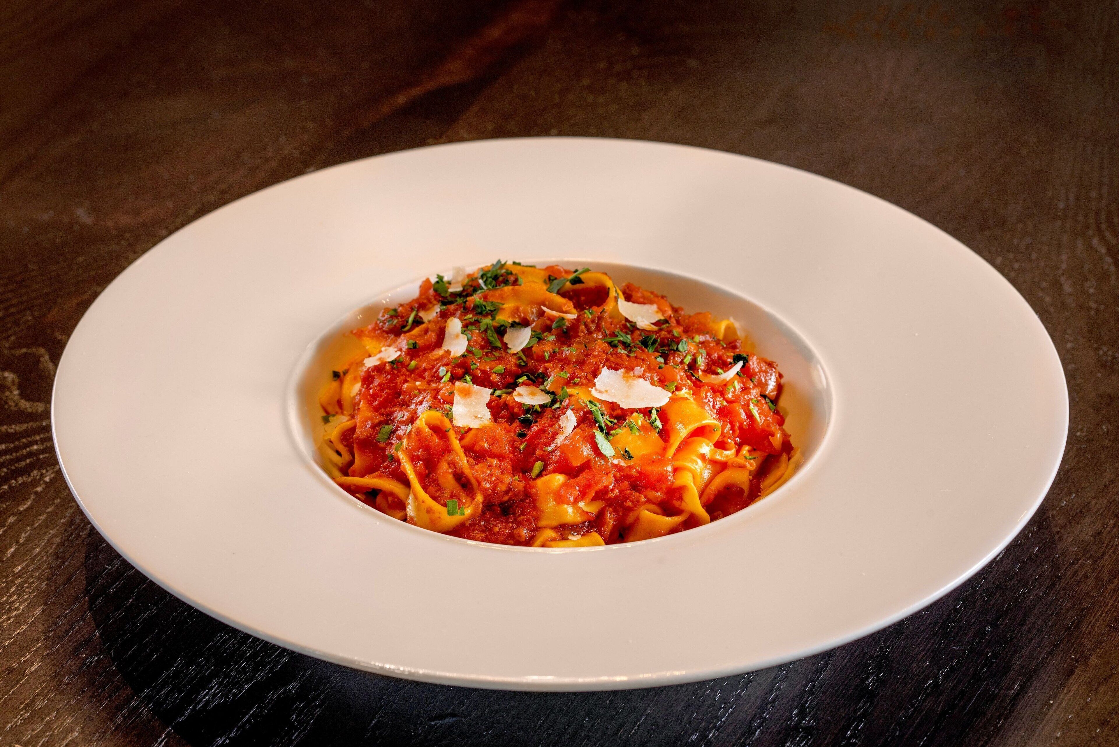 A white plate with pasta on a dark wooden table.