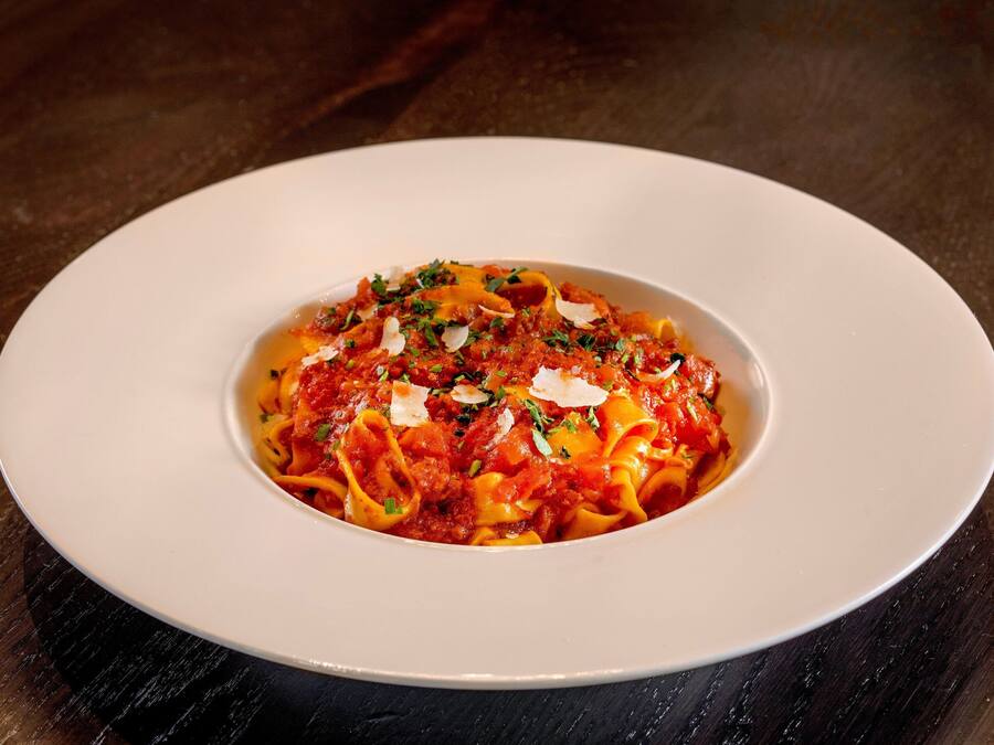 A white plate with pasta on a dark wooden table.