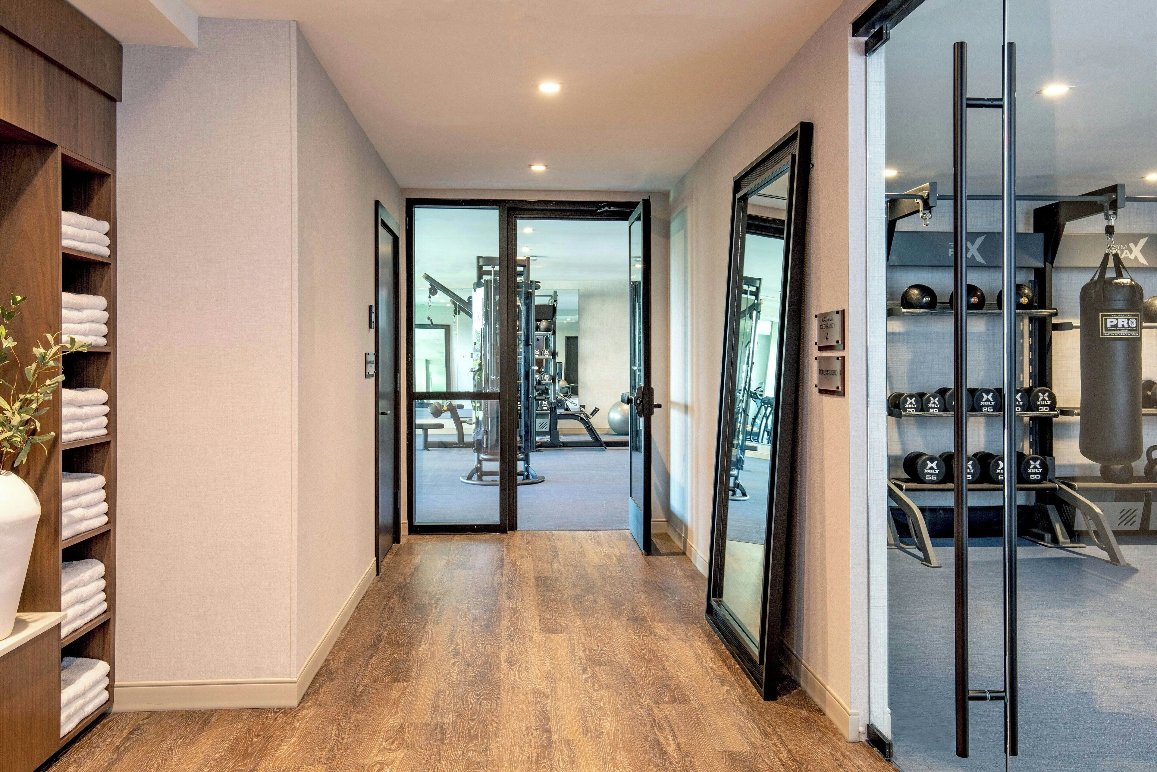 A hallway leading to a gym with exercise equipment, a wooden shelf with towels, and a punching bag.