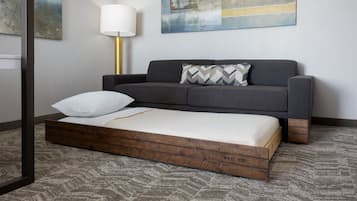 A modern room with a grey sofa, a wooden platform bed, a white pillow, a lamp, and abstract art on the wall.