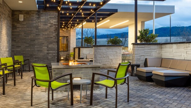 Eine Terrasse im Freien mit Ziegelboden, grünen Stühlen, einer Feuerstelle und einer modernen Lounge-Ecke.