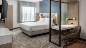 Ein Hotelzimmer mit Bett, Schreibtisch, Stuhl, Fernseher und einem fensterbepflanzten Fenster.